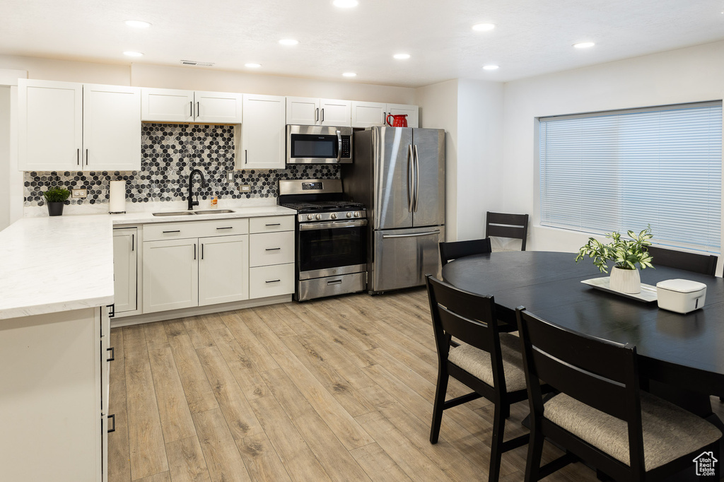 Kitchen featuring appliances with stainless steel finishes, light hardwood / wood-style flooring, tasteful backsplash, and sink