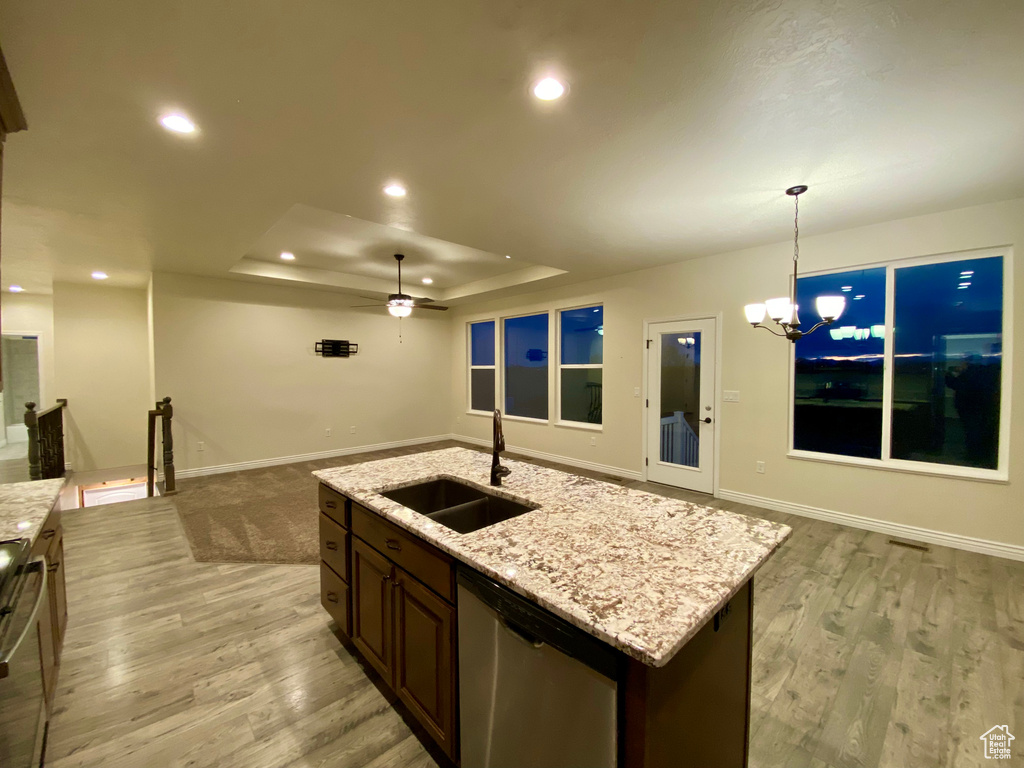 Kitchen featuring light stone countertops, ceiling fan with notable chandelier, sink, pendant lighting, and a tray ceiling