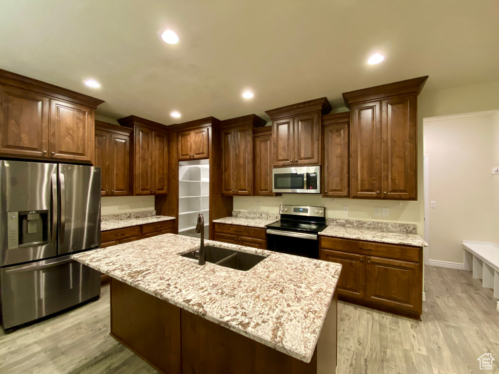Kitchen featuring light stone counters, a kitchen island with sink, light wood-type flooring, sink, and appliances with stainless steel finishes