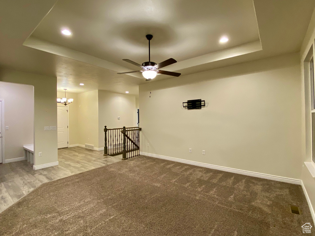 Carpeted empty room featuring ceiling fan with notable chandelier and a raised ceiling