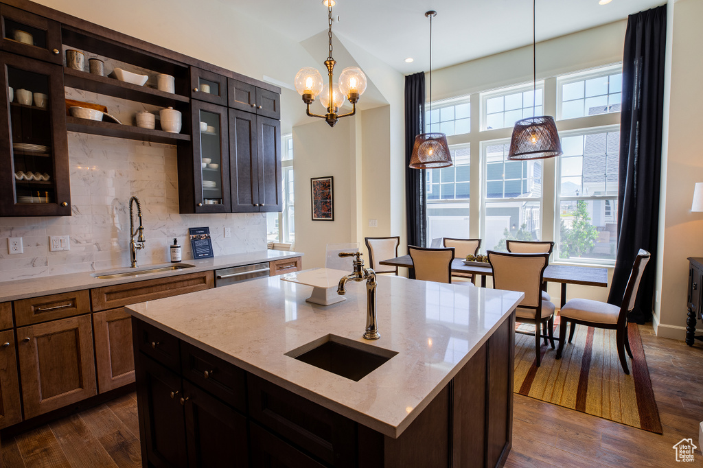 Kitchen featuring hanging light fixtures, a center island with sink, sink, and dark wood-type flooring