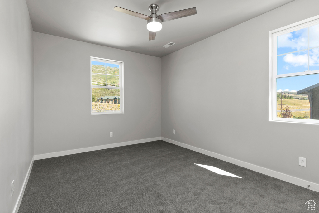 Empty room featuring ceiling fan and dark carpet