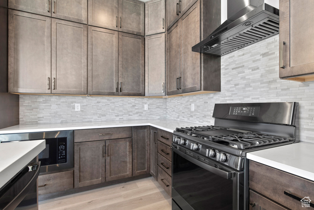 Kitchen with tasteful backsplash, light hardwood / wood-style flooring, wall chimney range hood, gas range, and black microwave