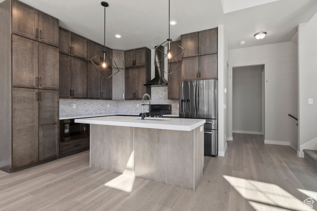 Kitchen with light hardwood / wood-style flooring, wall chimney exhaust hood, backsplash, and a kitchen island with sink