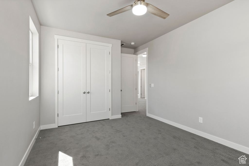 Unfurnished bedroom featuring dark carpet, a closet, and ceiling fan
