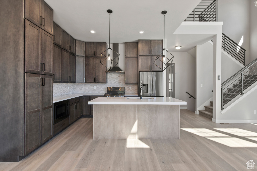 Kitchen with a center island with sink, light hardwood / wood-style flooring, wall chimney range hood, and stainless steel appliances