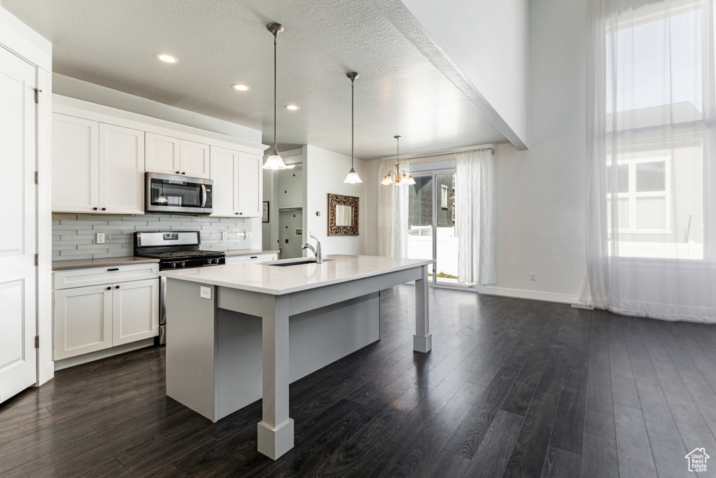 Kitchen with decorative light fixtures, a breakfast bar, a center island with sink, white cabinets, and dark hardwood / wood-style flooring