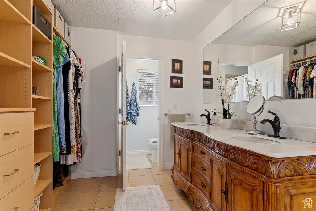 Bathroom with toilet, double sink vanity, a textured ceiling, and tile floors