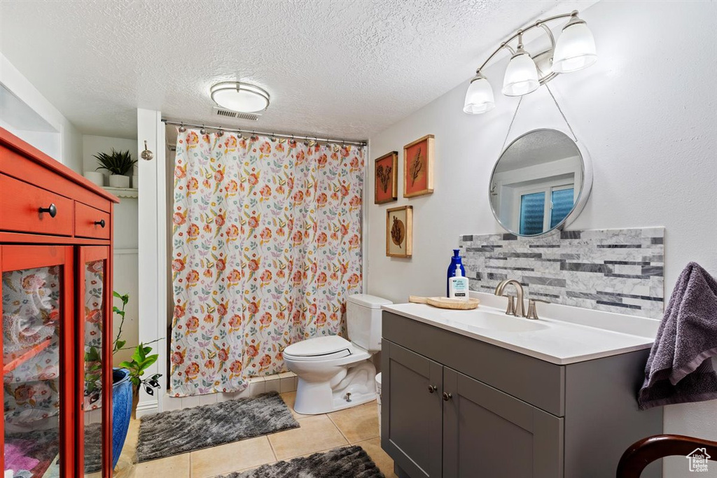 Bathroom featuring a textured ceiling, backsplash, vanity, toilet, and tile floors
