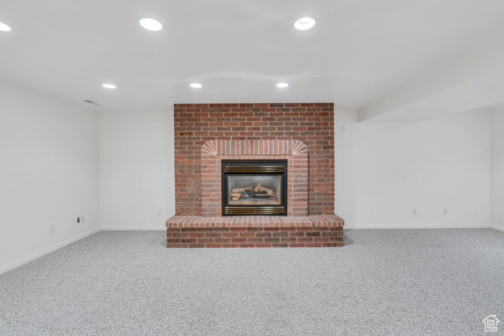 Unfurnished living room featuring brick wall, a fireplace, and carpet
