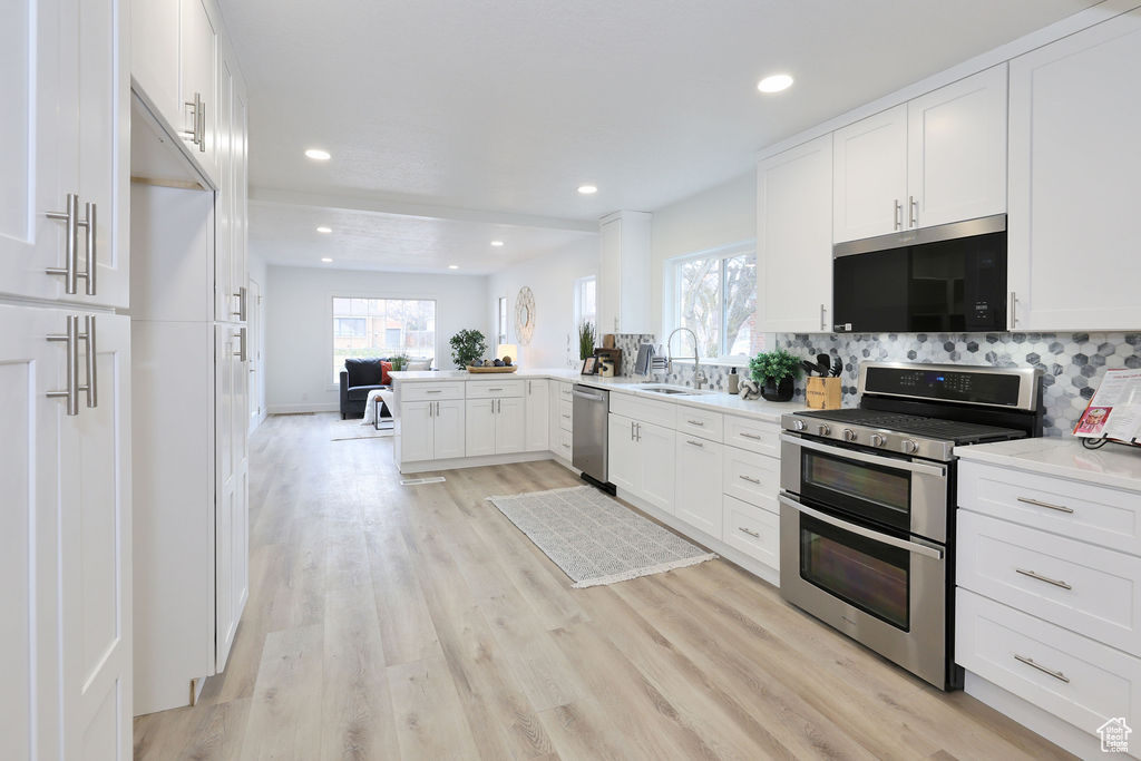 Kitchen with light hardwood / wood-style flooring, backsplash, white cabinets, sink, and stainless steel appliances