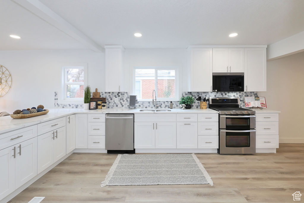 Kitchen featuring light hardwood / wood-style floors, backsplash, white cabinetry, sink, and stainless steel appliances