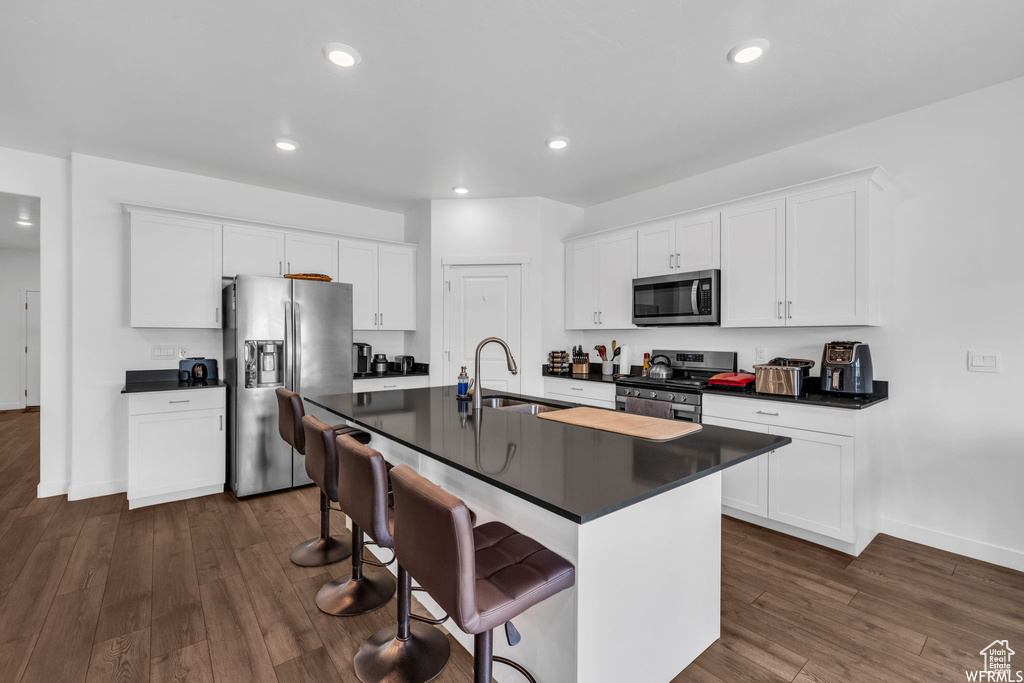 Kitchen featuring dark hardwood / wood-style flooring, stainless steel appliances, white cabinets, an island with sink, and sink