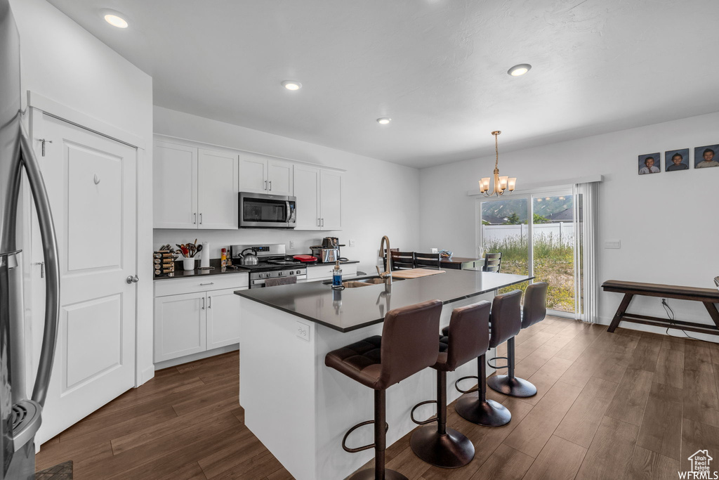 Kitchen with pendant lighting, stainless steel appliances, white cabinetry, a chandelier, and a kitchen island with sink