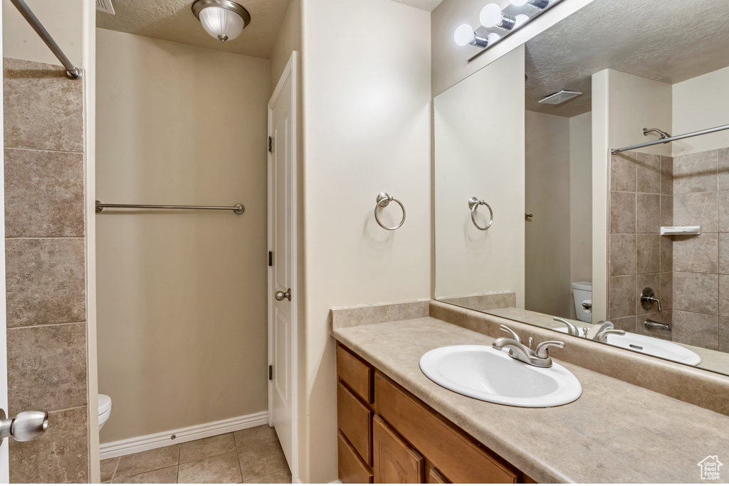Full bathroom featuring a textured ceiling, vanity with extensive cabinet space, tiled shower / bath, toilet, and tile flooring