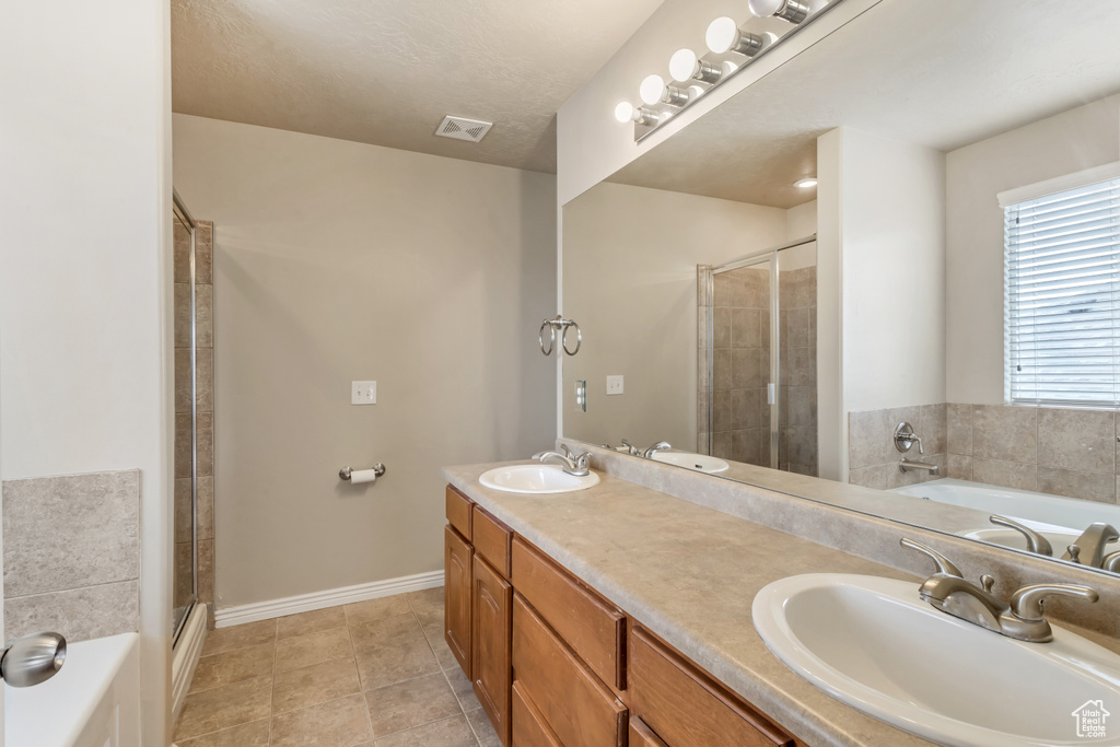 Bathroom featuring separate shower and tub, dual bowl vanity, and tile flooring