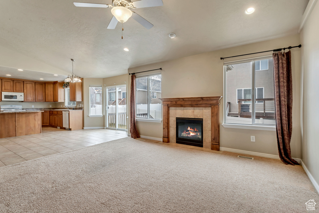 Unfurnished living room featuring ceiling fan with notable chandelier, light colored carpet, and a tile fireplace