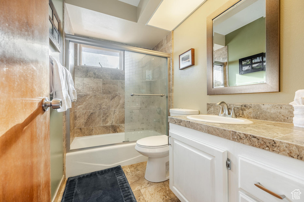 Full bathroom featuring enclosed tub / shower combo, tile floors, vanity, and toilet
