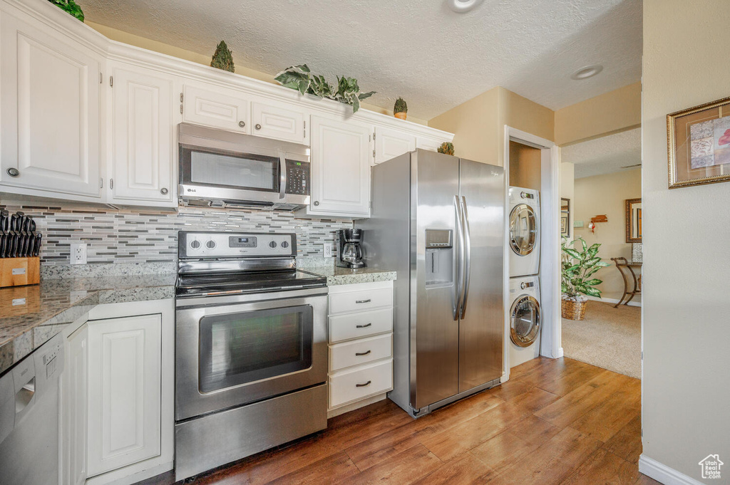 Kitchen with backsplash, light wood-type flooring, white cabinetry, stacked washing maching and dryer, and appliances with stainless steel finishes
