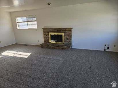 Unfurnished living room featuring a stone fireplace and carpet floors