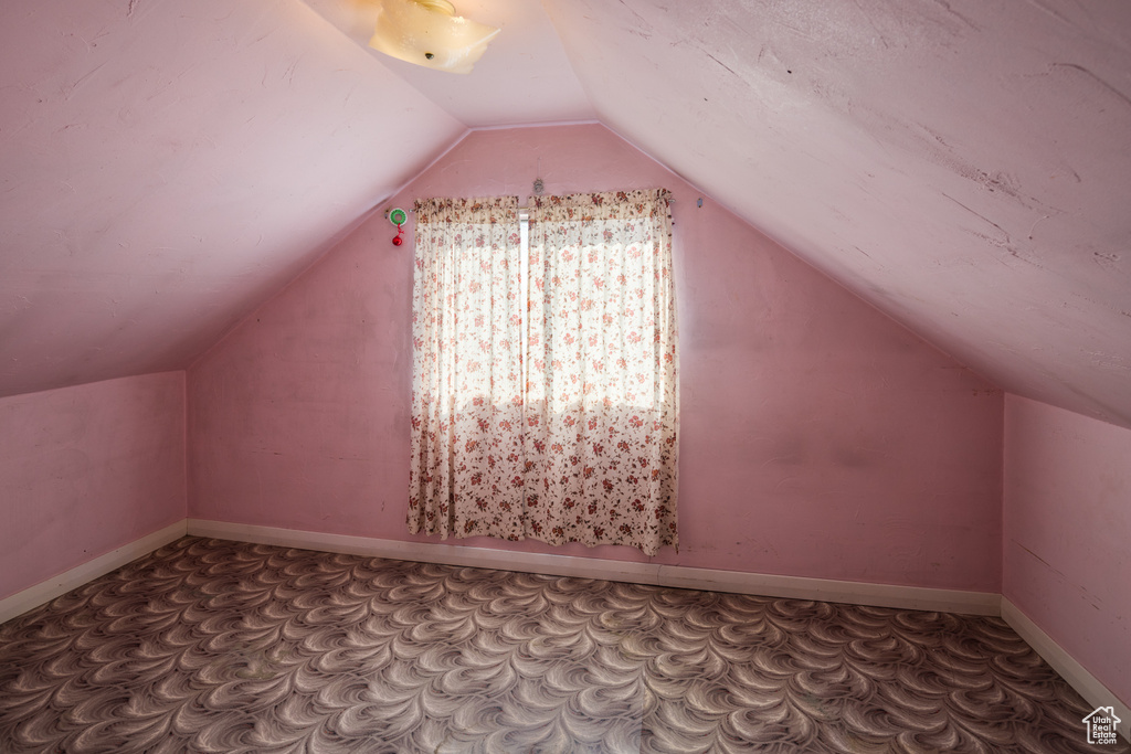Bonus room with dark carpet and vaulted ceiling