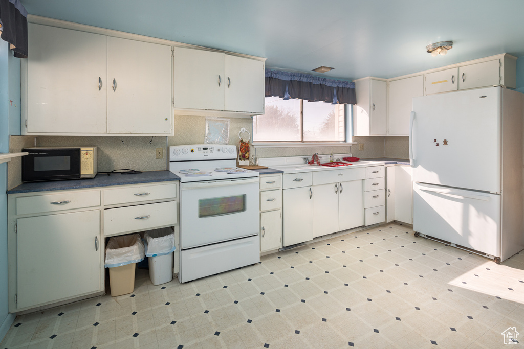Kitchen with white appliances, light tile floors, backsplash, and white cabinetry