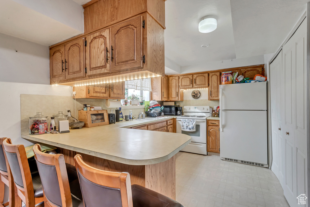 Kitchen featuring a breakfast bar, kitchen peninsula, white appliances, sink, and light tile floors