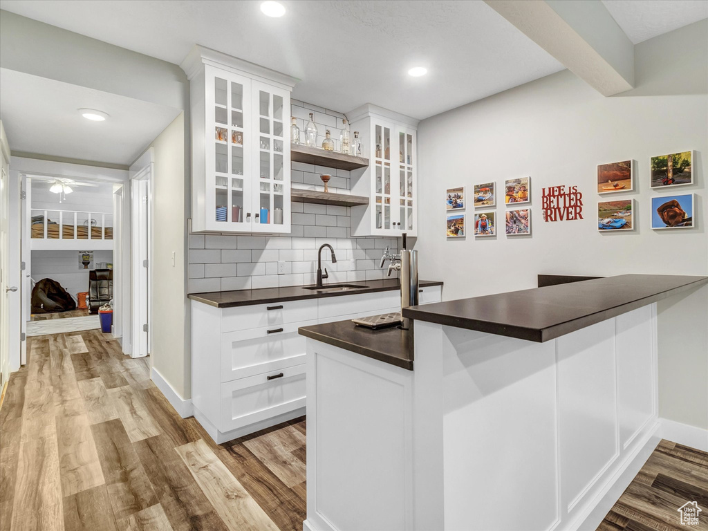 Kitchen with white cabinets, light hardwood / wood-style flooring, sink, and backsplash