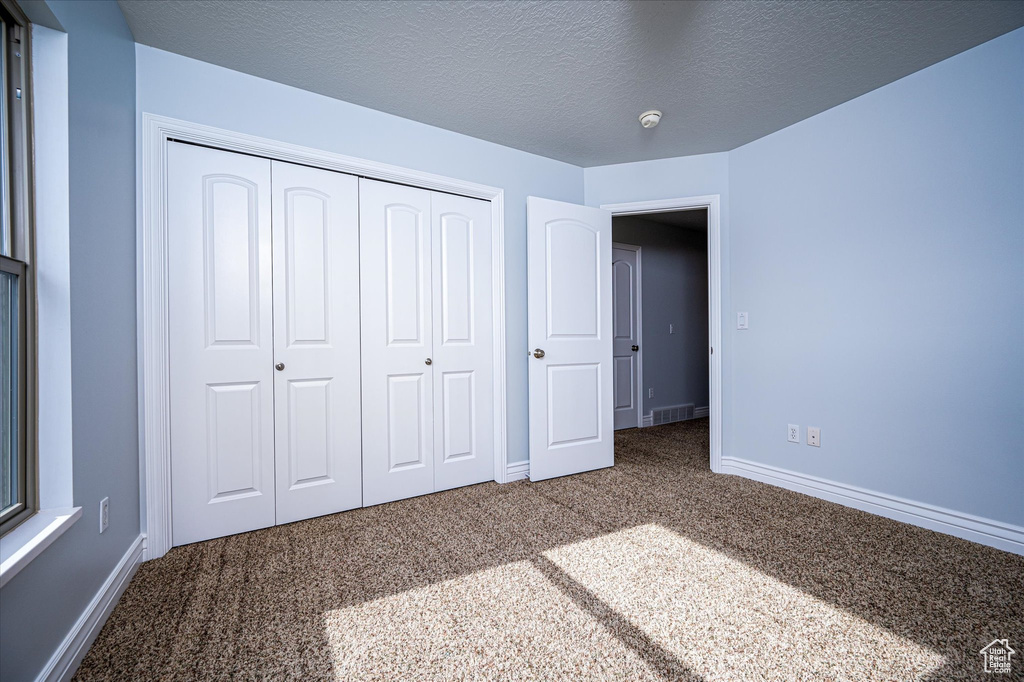 Unfurnished bedroom featuring a textured ceiling, dark carpet, and a closet