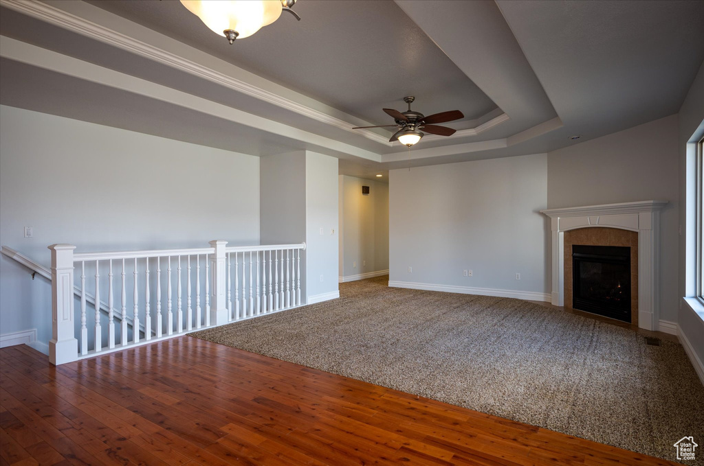 Interior space with a tiled fireplace, crown molding, dark wood-type flooring, ceiling fan, and a tray ceiling