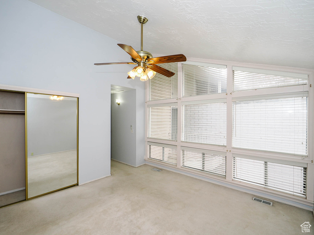 Unfurnished bedroom with high vaulted ceiling, ceiling fan, light colored carpet, and a closet
