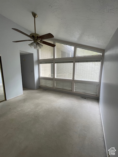 Empty room with vaulted ceiling, a textured ceiling, ceiling fan, and carpet floors