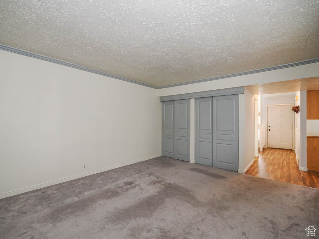 Unfurnished bedroom with crown molding, light carpet, a textured ceiling, and a closet