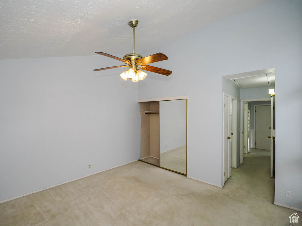 Unfurnished bedroom with a closet, ceiling fan, light colored carpet, and lofted ceiling