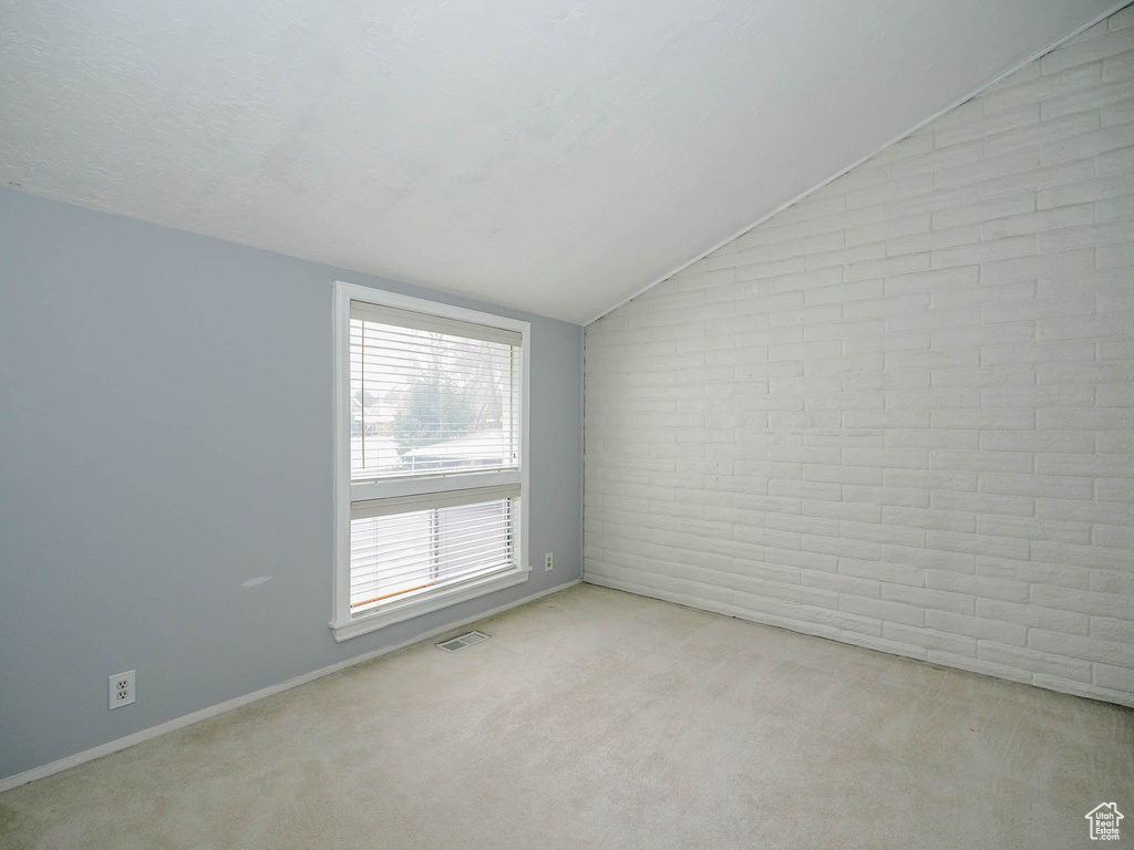 Carpeted empty room with brick wall and lofted ceiling