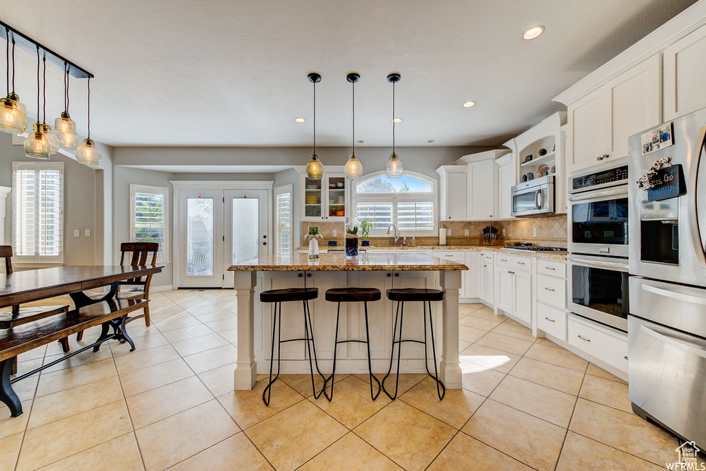 Kitchen featuring white cabinets, a kitchen island, stainless steel appliances, and decorative light fixtures