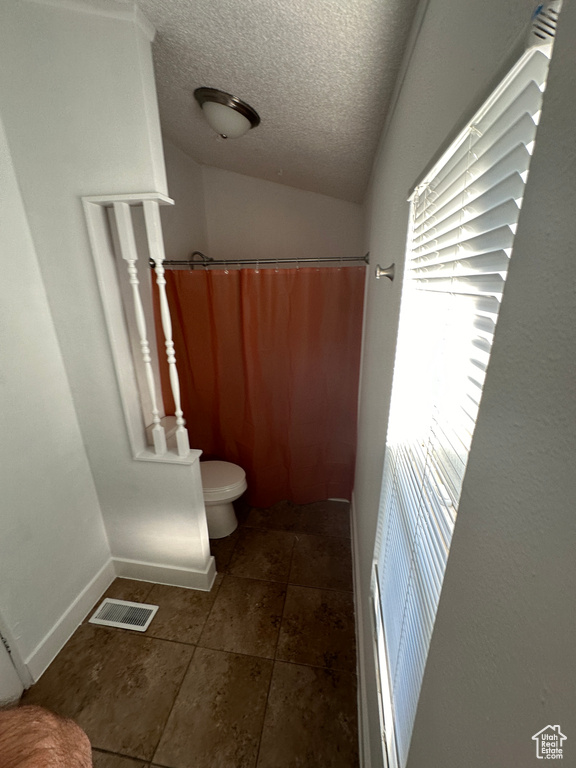 Bathroom featuring toilet, a textured ceiling, tile floors, and vaulted ceiling