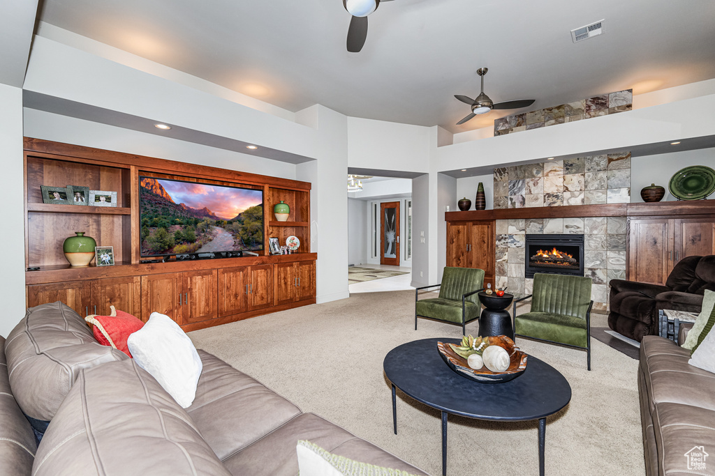 Carpeted living room with a stone fireplace, ceiling fan, and built in features