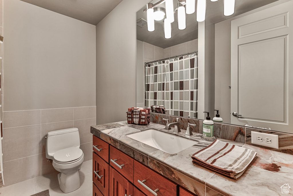 Bathroom with toilet, tile walls, tile flooring, and vanity with extensive cabinet space