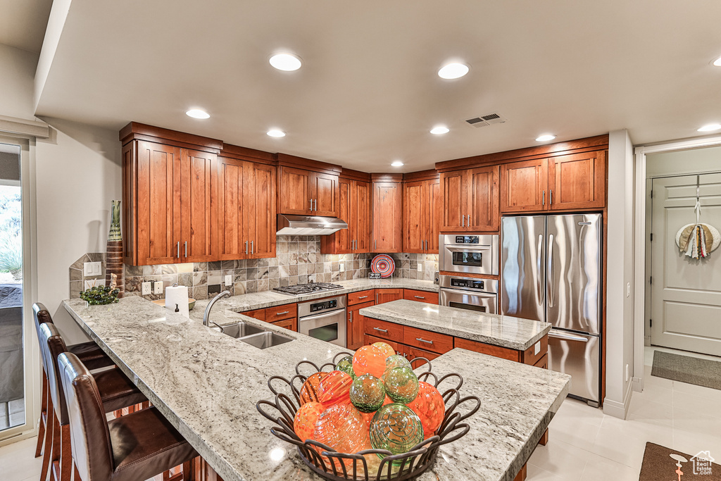 Kitchen featuring a kitchen bar, tasteful backsplash, sink, light tile floors, and appliances with stainless steel finishes