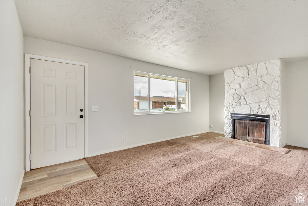 Unfurnished living room with light carpet and a stone fireplace