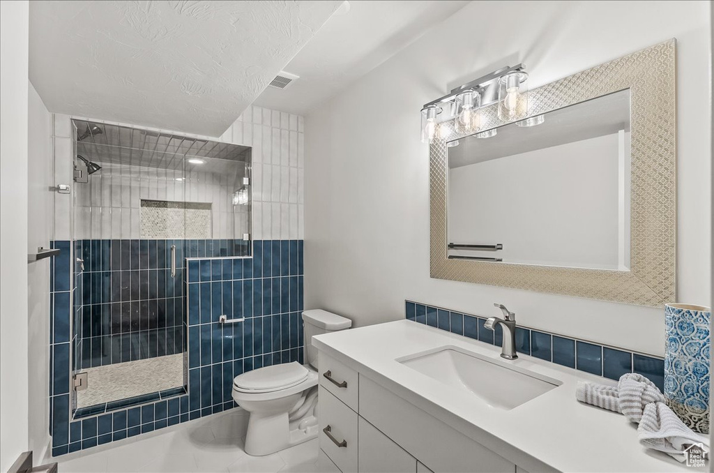 Bathroom featuring oversized vanity, toilet, tile walls, tile flooring, and a tile shower