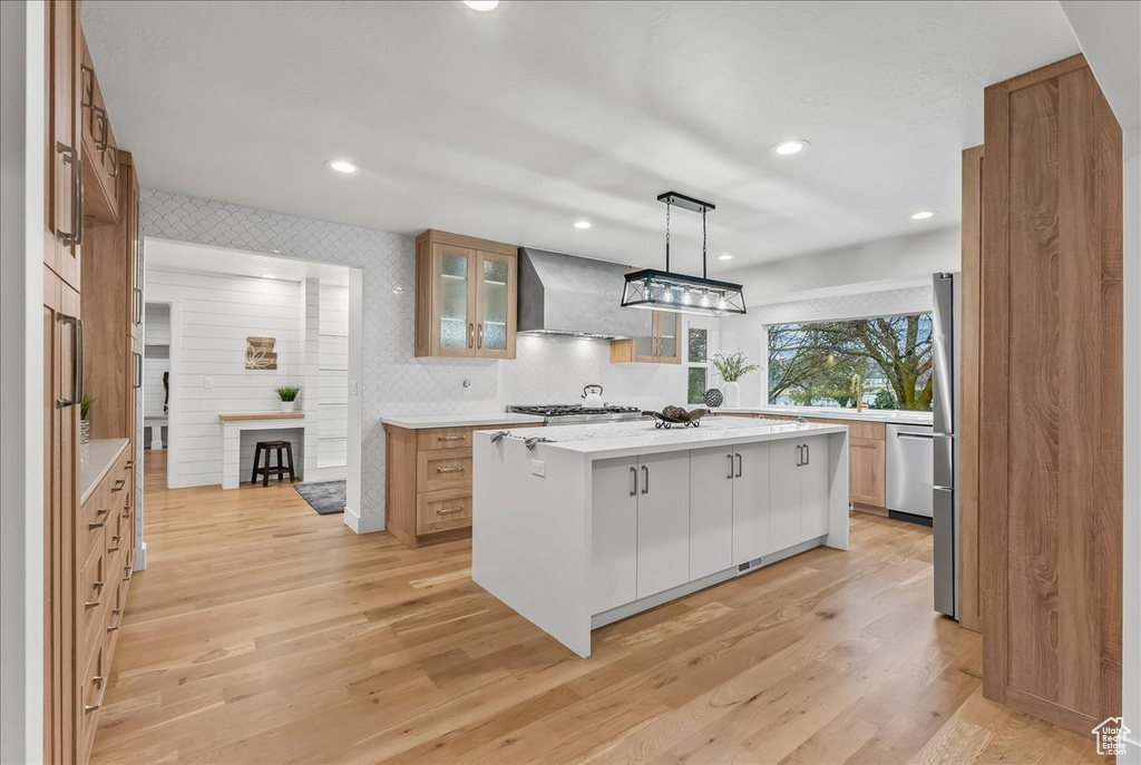 Kitchen featuring a center island, hanging light fixtures, wall chimney exhaust hood, and light wood-type flooring