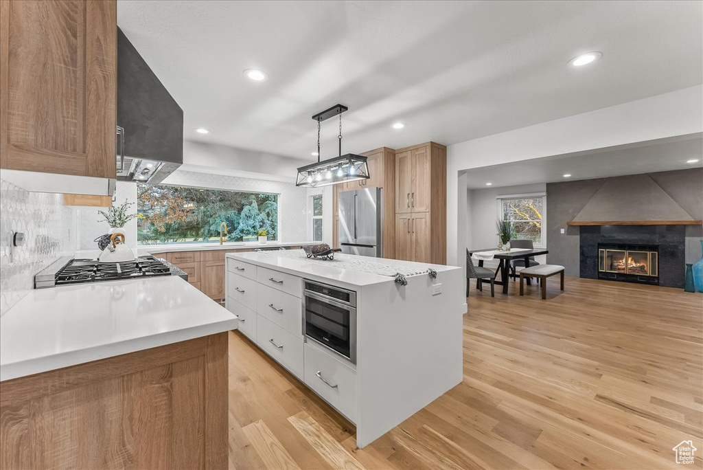 Kitchen featuring light wood-type flooring, white cabinets, a center island, stainless steel appliances, and decorative light fixtures