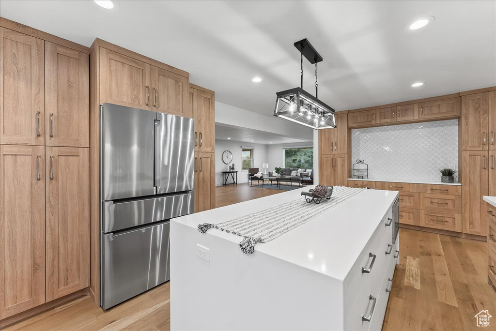 Kitchen featuring light hardwood / wood-style floors, decorative light fixtures, backsplash, and stainless steel fridge