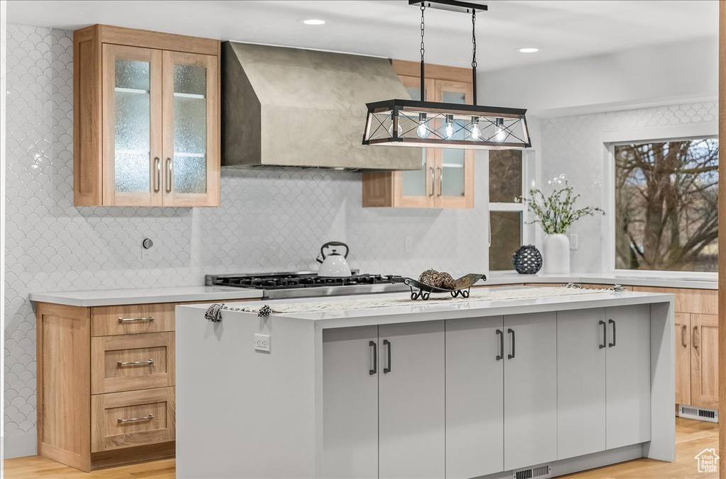 Kitchen with light hardwood / wood-style floors, hanging light fixtures, light stone countertops, custom range hood, and tasteful backsplash