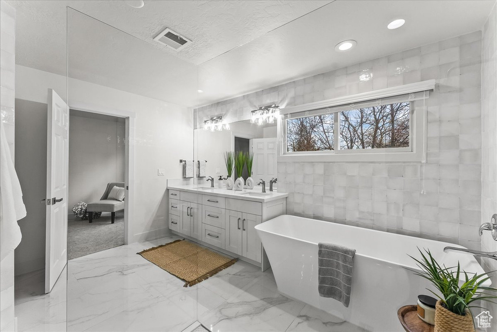 Bathroom featuring a bathtub, tile walls, double sink, large vanity, and tile flooring