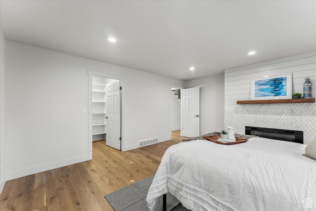 Bedroom with light hardwood / wood-style floors, a walk in closet, a tiled fireplace, and a closet