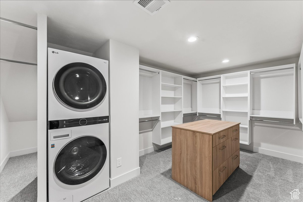Laundry room with stacked washer and dryer and light colored carpet