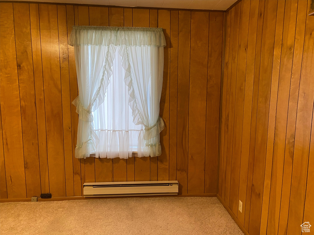 Empty room with a baseboard radiator, light carpet, and wood walls